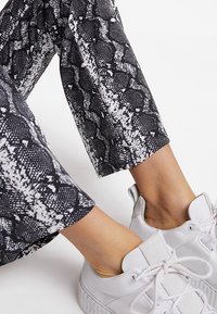 Pantaloni a stampa serpente bianco e nero con vestibilità slim abbinati a sneakers bianche low-top, dotate di lacci arrotondati e suola texturizzata.