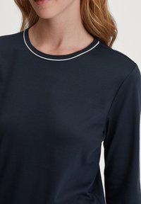 Marineblauwe longsleeve top met een ronde halslijn en witte bies, gemaakt van zachte, gladde stof. Sluit nauw aan rond de halslijn.
