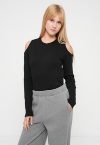 Top negro de manga larga con hombros descubiertos, textura acanalada, cuello redondo, combinado con pantalones deportivos gris de corte relajado y pretina.