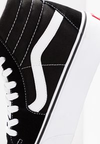 Sneaker alta bianca e nera con lacci bianchi, dettaglio a striscia bianca e suola spessa bianca su uno sfondo semplice.