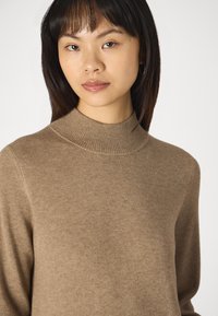 Pullover marrone lavorato a maglia con colletto rialzato e texture a costine, caratterizzato da una vestibilità comoda e un materiale morbido. Il colore è ricco e caldo.