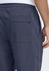 Navy blue cotton pants featuring an elastic waistband, side pockets, and a large back patch pocket. Smooth texture with a relaxed fit.