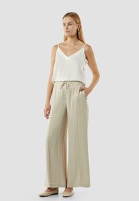 Lichtgewicht witte top met spaghettibandjes, gecombineerd met beige wijde broek met een trekkoord in de taille en zijzakken.