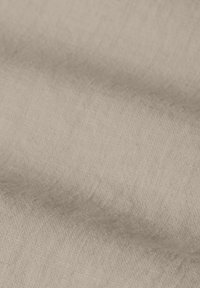 Vue rapprochée d'un tissu beige froissé avec une texture tissée visible et des plis doux.