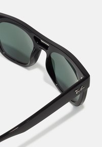 Ochelari de soare Black Ray-Ban cu lentile verzi, un cadru gros și elegant și un mic logo pe lateral, care evidențiază un design modern.
