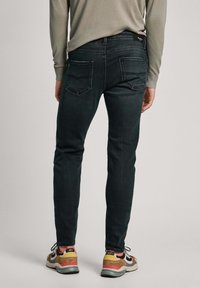 Person som bär mörka slim fit-jeans och flerfärgade sneakers, visad bakifrån mot en enfärgad bakgrund.