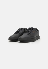 Baskets noires en matériau synthétique lisse avec un bout arrondi, un design à lacets et un branding subtil sur le côté.