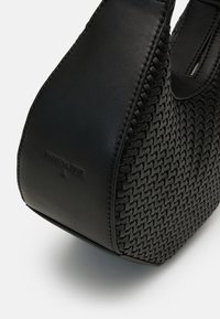 Borsa a mano in pelle nera caratterizzata da una trama intrecciata, forma curva e logo impresso. La superficie liscia contrasta con il dettaglio intrecciato complesso.