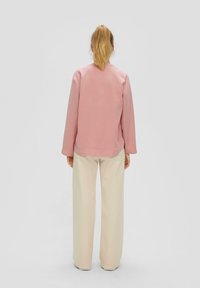 Maglietta rosa a maniche lunghe con scollatura rotonda, abbinata a pantaloni larghi color beige chiaro, mostrata da dietro. Texture del tessuto morbidosa evidente.