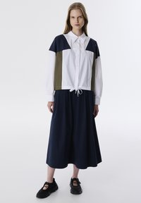 Robe à blocs de couleurs présentant un design blanc, marine et olive, avec un devant à boutons, des manches longues et un ourlet avec cordon de serrage. Portée avec des baskets noires.