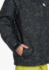 Svart jacka med grönt klottermönster, försluten med dragkedja fram, sidofickor och kardborrefästen vid ärmsluten. Vattentåligt tyg med slät textur.