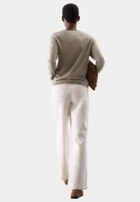 Suéter de punto beige, pantalones anchos blancos, bolso marrón y botines. Vista desde la parte de atrás que muestra un corte relajado y texturas suaves.