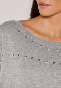 Grau pullover aus weichem Material, mit metallischen Nieten entlang des Halsausschnitts und Saums. Das Design umfasst einen weiten Rundhalsausschnitt und gerippte Kanten.