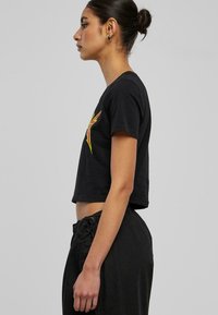 Tricou scurt negru cu mâneci scurte, având un design grafic multicolor. Modelul poartă pantaloni negri cu șnur, evidențiind o siluetă ajustată.