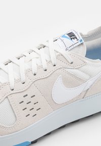 Nike-sneakers med en överdel i beige mocka och mesh, vita detaljer, grå snören och en ljusblå sula; har perforerade detaljer.
