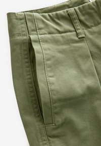 Gros plan sur un pantalon vert en coton montrant la taille, la passants de ceinture, la poche latérale et les coutures détaillées sur le tissu.