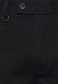 Pantaloni neri in cotone con chiusura a bottone, passanti per cintura, tessuto strutturato con righe diagonali e tasche laterali.