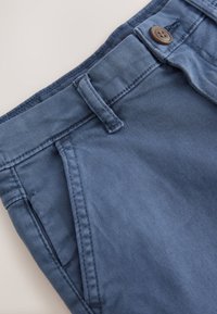 Pantalones de tela de algodón azul oscuro con cintura clásica, cierre de botón y bolsillos laterales con detalles de costuras en tono.