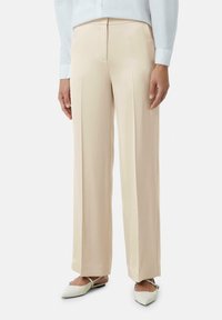 Beige op maat gemaakte broek met een vloeiende, soepele textuur, voorzien van voorplooien en een rechte pijp. Gecombineerd met lichtgroene puntige flats.