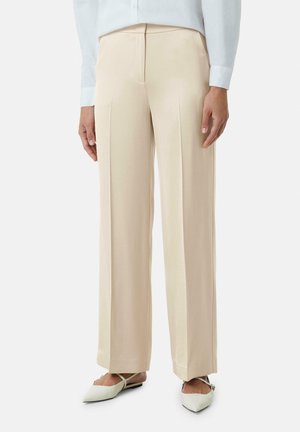 Beige op maat gemaakte broek met een vloeiende, soepele textuur, voorzien van voorplooien en een rechte pijp. Gecombineerd met lichtgroene puntige flats.