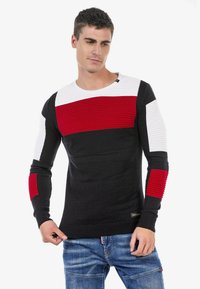 Schwarzer und weißer Strickpullover mit roten horizontalen Streifen. Gerippte Textur an den Ärmeln und Schultern, runder Halsausschnitt und taillierte Passform.