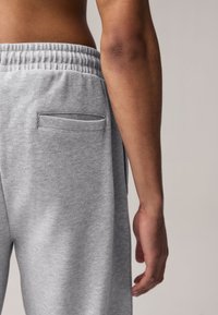 Gray textured sweatpants with an elastic waistband, featuring a single back pocket and a close-up of a bare arm beside them.