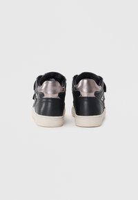 Sorte lær sneakers med metallisk sølvdetaljer, en teksturert hæl og såle av hvitt gummi. Har borrelåsremmer for lukking.