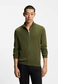Maglione verde in maglia con zip, maniche lunghe, collo alto e polsini a coste. Logo sul petto e dettaglio contrastante all'interno del collo.