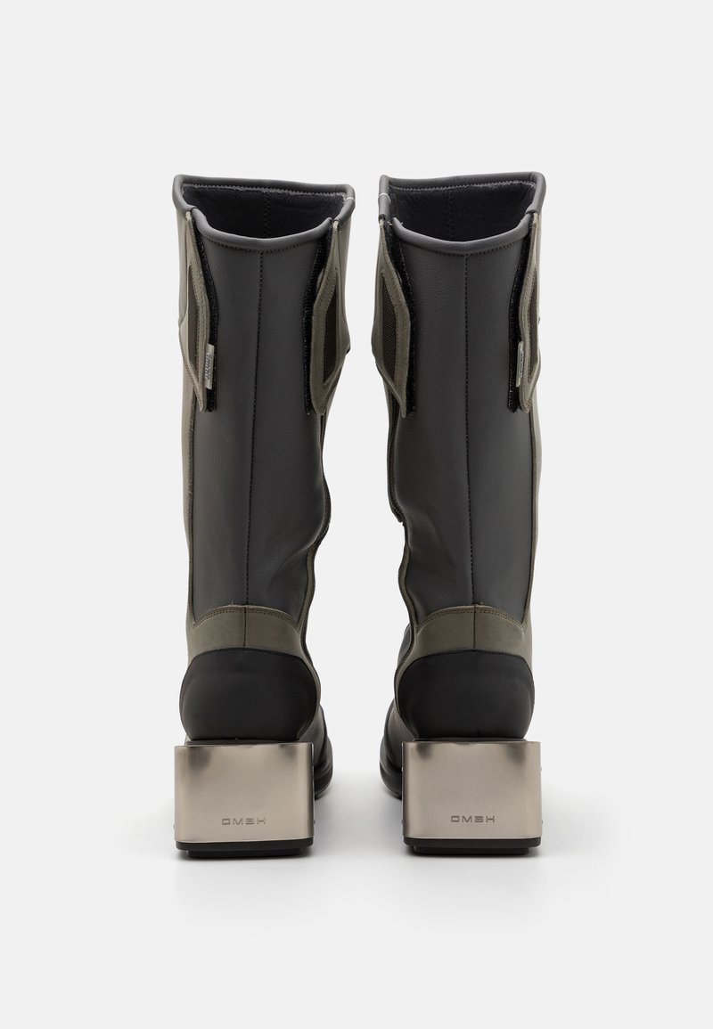 Grijze waterdichte laarzen met een hoge schacht, zwarte rubberen neuskap en metallic blokhak. Mesh zijkanten voor ventilatie.