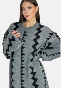 Overzichtige grijze gebreide trui met zwarte zigzagpatronen, een geribde halslijn en wijde, vloeiende mouwen. Textiele en gezellige stof.