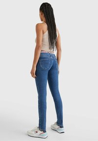 Niebieskie dżinsowe rurki z średnim stanem, z charakterystycznym wzorem kieszeni z tyłu i markowym paskiem. Zestawione z białymi trampkami.