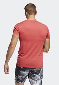 Rød atletisk t-shirt med et tekstureret mønster, korte ærmer og en tætsiddende pasform, båret med sorte og hvide mønstrede shorts.