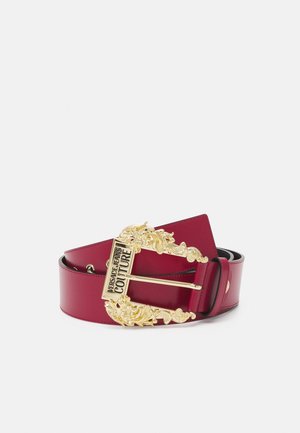 Cinturón de cuero rojo oscuro enrollado con una hebilla dorada ornamentada con diseños florales y texto "Versace Jeans Couture".