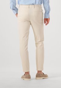 Beige katoenen broek met een slim fit, voorzien van twee achterzakken, riemlussen en een enkel-lange zoom. G gedragen met lichtbruine instapschoenen.