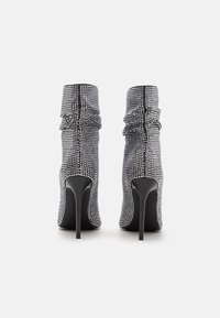 Stivaletti neri con tacco alto alla caviglia, esterno tempestato di strass e dettaglio in tessuto arricciato sulla parte superiore. Silhouette elegante e affusolata.