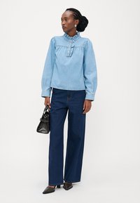 Ανοιχτό μπλε τζιν μπλούζα με ριγωτό γιακά και κουμπιά, σε συνδυασμό με σκούρα μπλε τζιν φάρδους. Συνοδευμένη με μικρή μαύρη τσάντα.