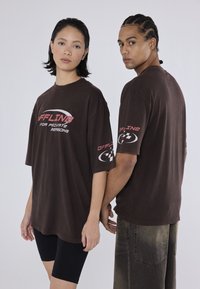 Brune oversized t-shirts har rød og hvid tekst, "OFFLINE FOR PRIVATE REASONS," samt logodetaljer på ærmerne. Modellerne har sorte shorts på.