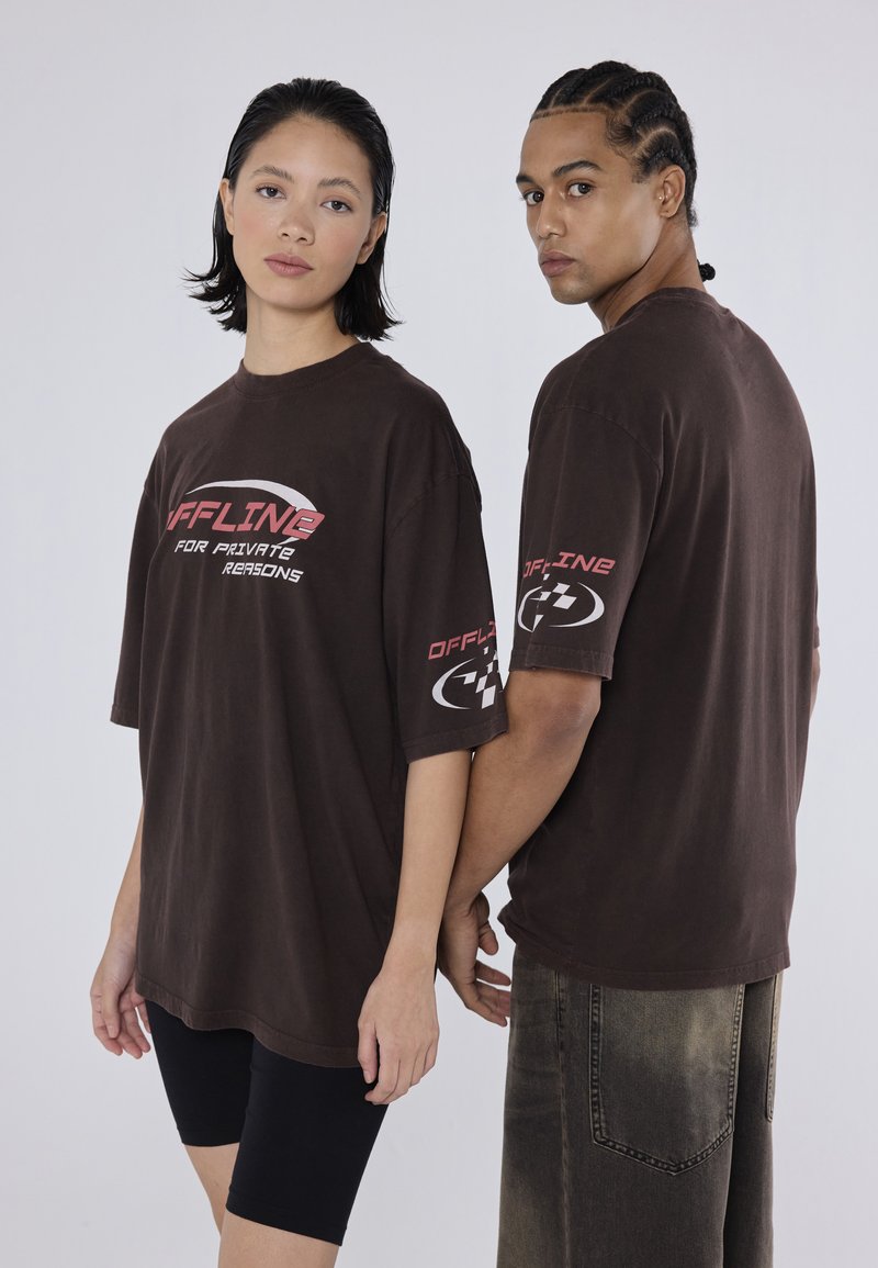 Brune oversized t-shirts har rød og hvid tekst, "OFFLINE FOR PRIVATE REASONS," samt logodetaljer på ærmerne. Modellerne har sorte shorts på.