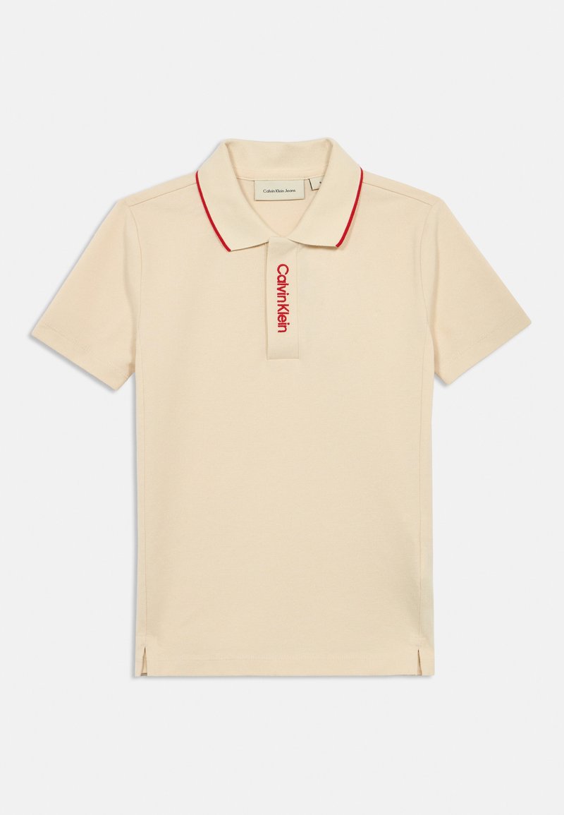 Béžová polo tričko s červeným golierom a vyšitým logom "Calvin Klein" na ľavej hrudi. Krátke rukávy, bočné rozparky na leme.