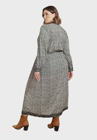 Långärmad klänning med svart-vit mönster och samlad baksida, som har en flytande silhuett och svarta accenter vid fåll och ärmslut. Bruna klackstövlar.