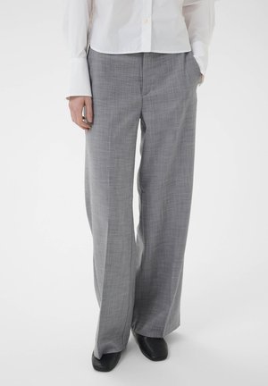 White long-sleeve shirt and gray wide-leg trousers worn by a person standing with one hand in pocket and black shoes visible.