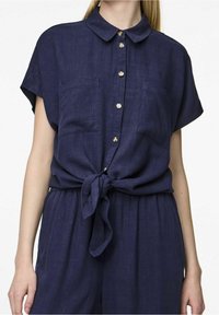 Camicia di lino blu navy a maniche corte con colletto, cinque bottoni frontali, due tasche sul petto e un dettaglio annodato in vita.