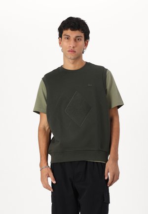 Dark green sleeveless sweatshirt with textured diamond design and logo, paired with short-sleeve olive shirt underneath. Cotton blend material.