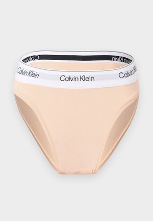 Ανοιχτό μπεζ ανδρικό εσώρουχο Calvin Klein με λευκή ελαστική ζώνη μέσης που φέρει μαύρο λογότυπο "Calvin Klein", σε ουδέτερο φόντο.