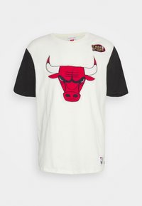 Bílý tričko s výraznou grafikou červeného býka na přední straně, černé krátké rukávy a malou nášivkou NBA Finals 1998 na rameni.