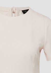 Lichtbeige top met korte mouwen, een ronde hals en een knoopdetail aan de achterkant van de kraag.