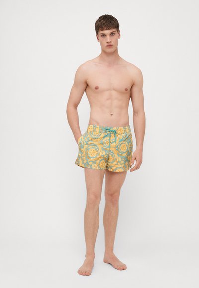 Shorts de bain pour hommes en tissu teal clair avec des motifs floraux jaunes. Dotés d'une taille élastique avec cordon de serrage et de poches latérales.
