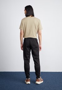 Camiseta beige de manga corta combinada con pantalones joggers negros que presentan franjas laterales blancas, cinturilla elástica y dobladillos negros. Zapatillas marrones.