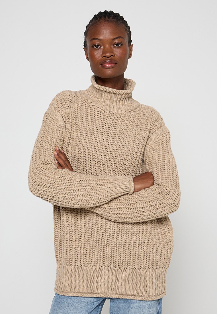Beżowy sweter dzianinowy z wysokim kołnierzem, luźnym krojem i teksturowanym wzorem. Długie rękawy ze ściągaczami i u dołu. Casualowy design, gruba przędza.