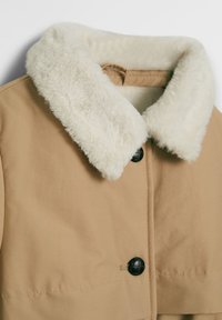 Beige Jacke mit einem weichen weißen Kunstfellkragen, schwarzem Knopfverschluss und glatter Textur. Das Design betont Wärme und Komfort.
